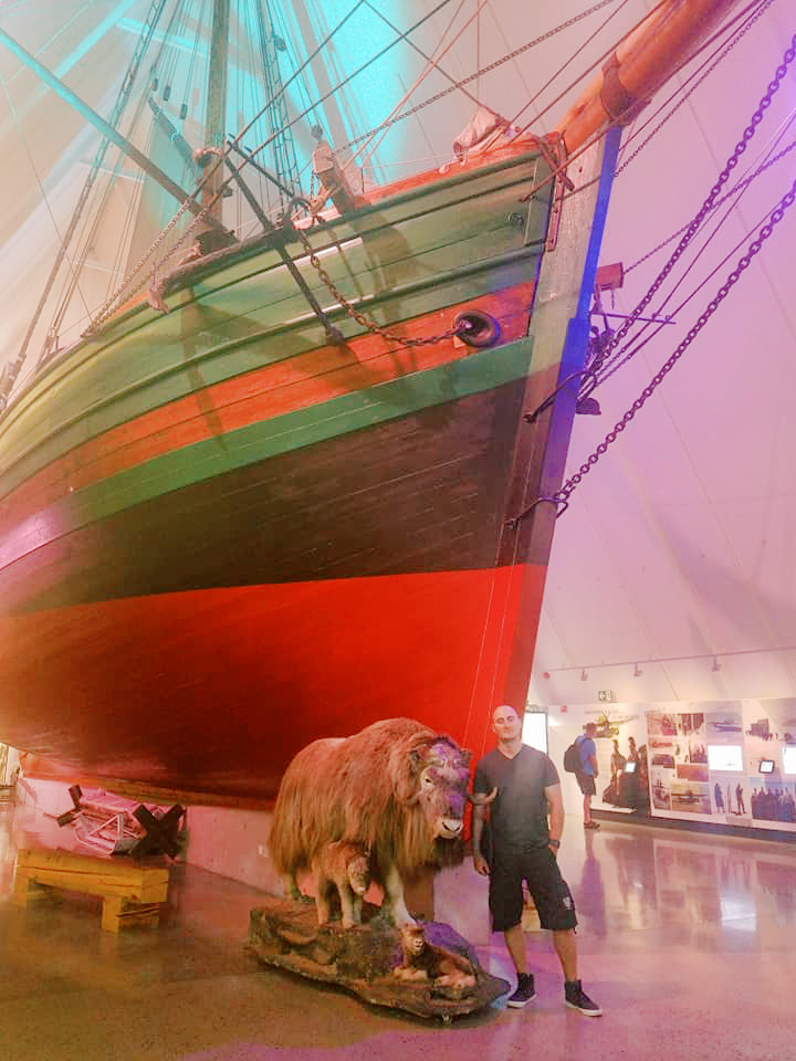 A man stands next to figures of ox beneath a large model ship in a museum 