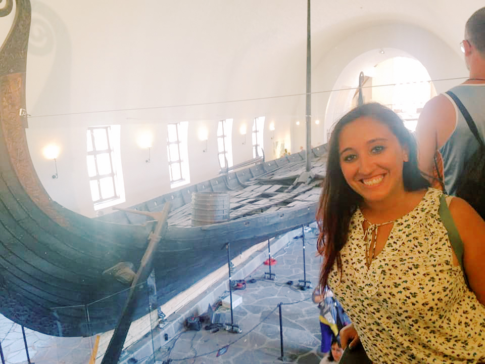 A woman smiles beside an excavated Viking ship on display in a museum