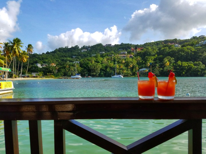 Two glasses of red rum punch in front of Marigot Bay, St Lucia. These are the perfect drinks to have during a trip to St Lucia with a friend