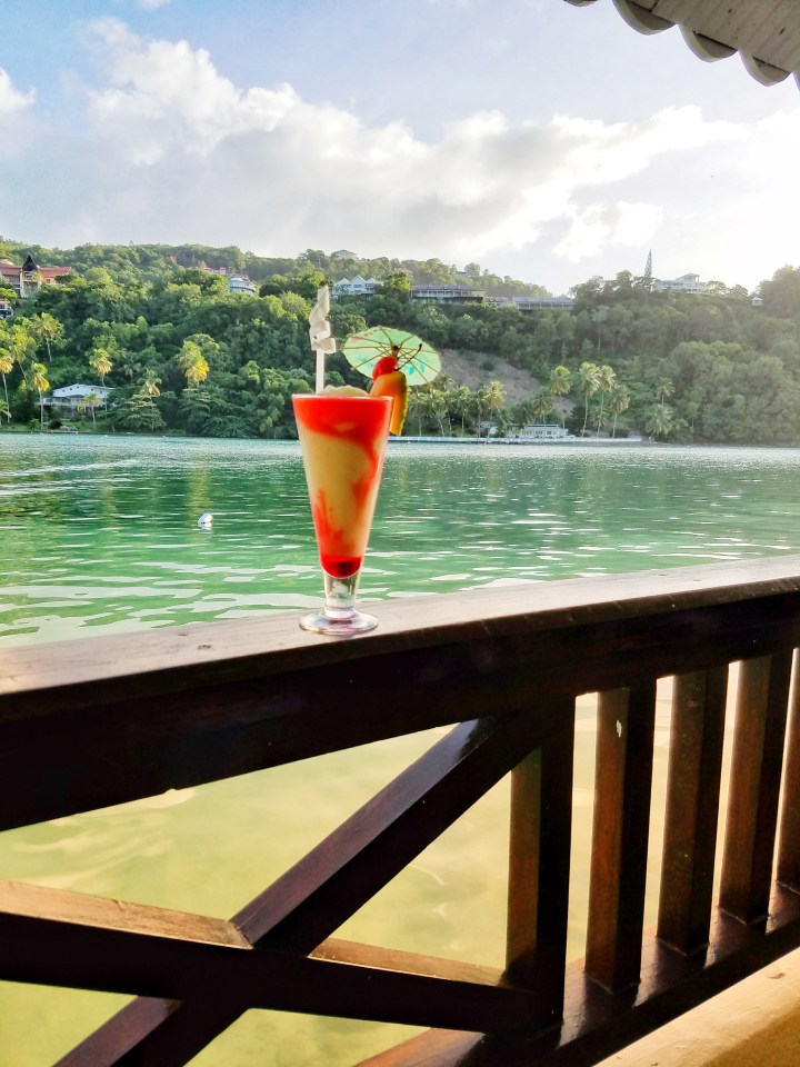 A beverage lies on a deck railing overlooking the waters of St Lucia