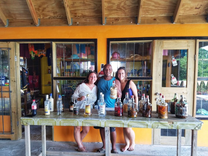 Two women stand on either side of a rum procurer during their one day trip to Soufriere. 