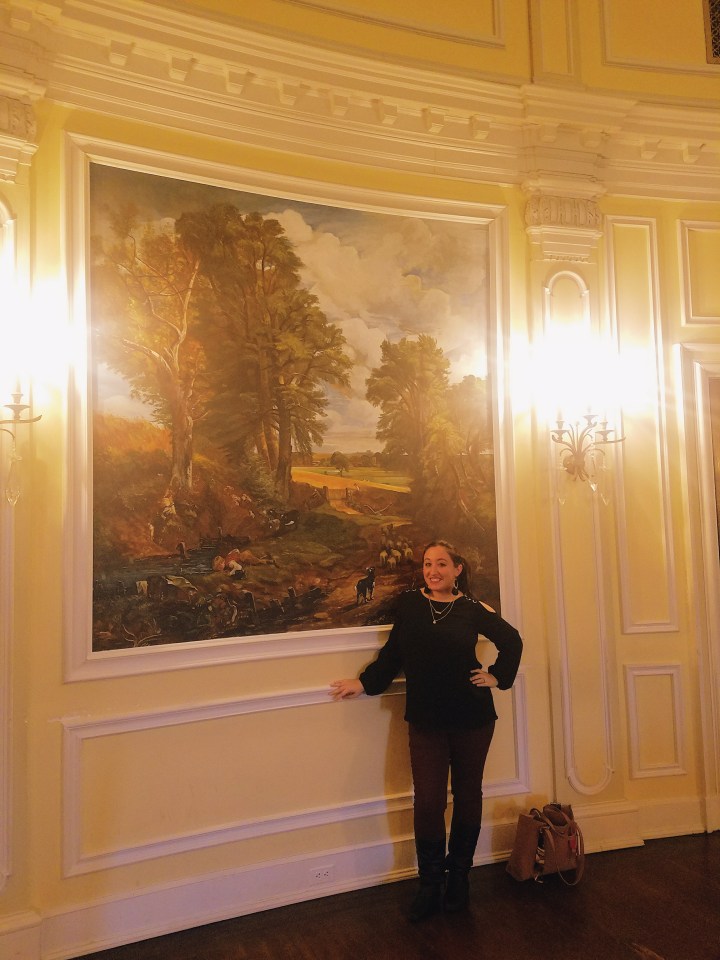 standing by a giant mural in the Oheka Castle on Long Island, the inspiration for Gatsby's mansion
