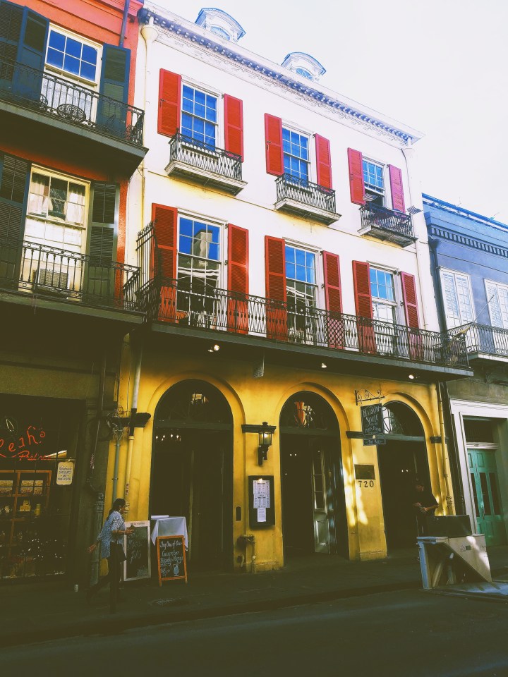 A yellow two story building with red shutters showing the famous architecture of New Orleans