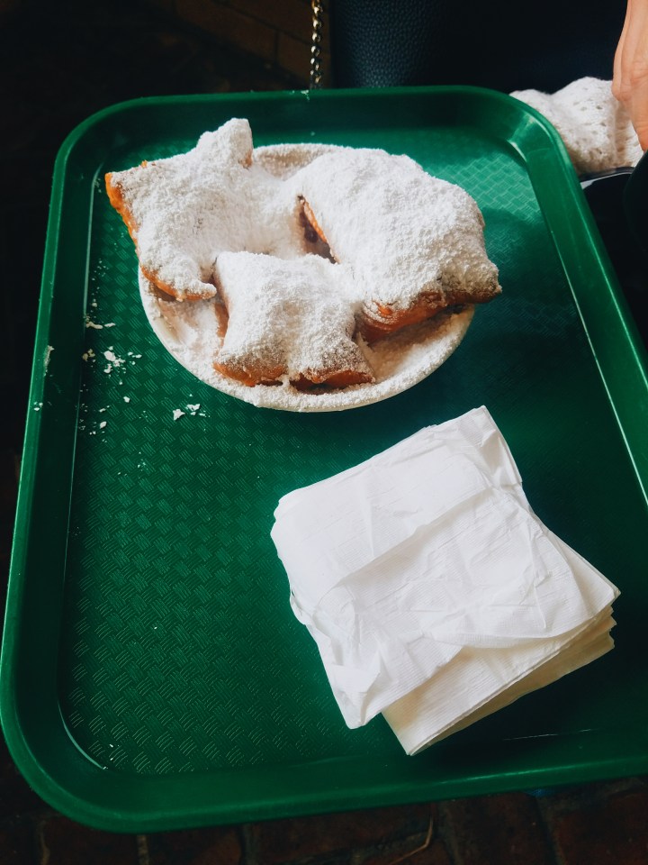 Three beignets covered in powder sugar on a green tray with napkins. 