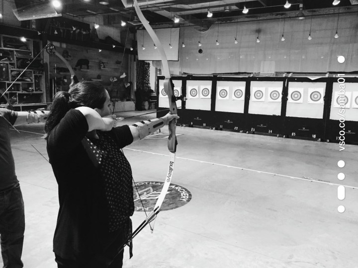Woman draws a bow backward ready to shoot an arrow at a target during archery lesson at Gotham Archery in Brooklyn