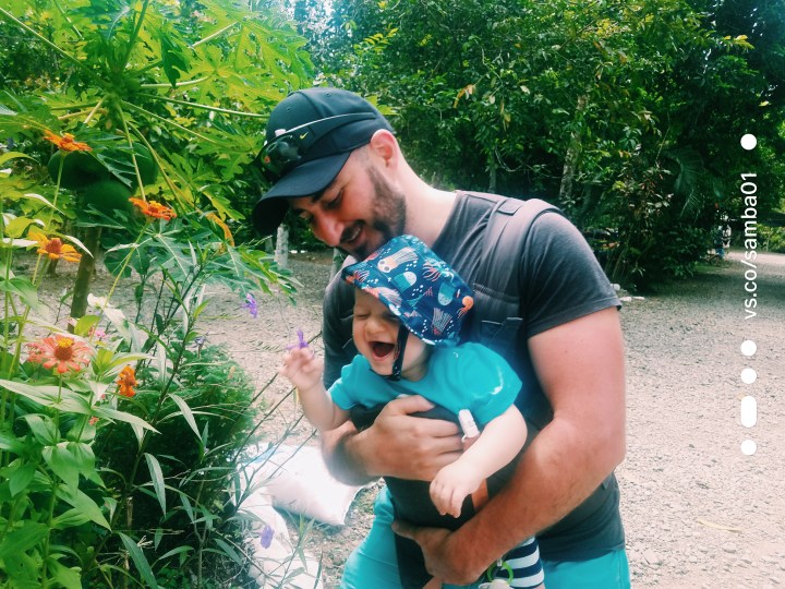 A father holds his baby who is laughing as he smells a bunch of flowers