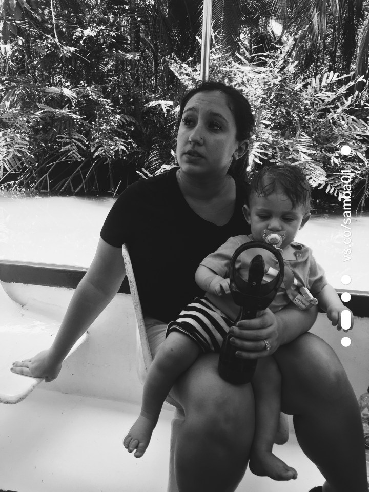 A tired mother and her baby son sit on a boat on the waterways of Costa Rica on the monkey boat tour. The baby is playing with a small portable fan