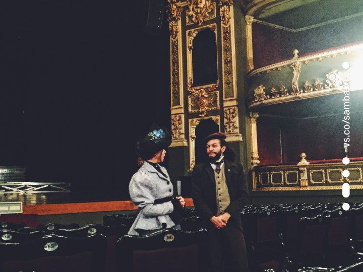 Two tour guides of the Teatro Nacional stand looking at each other dressed in period clothing. 