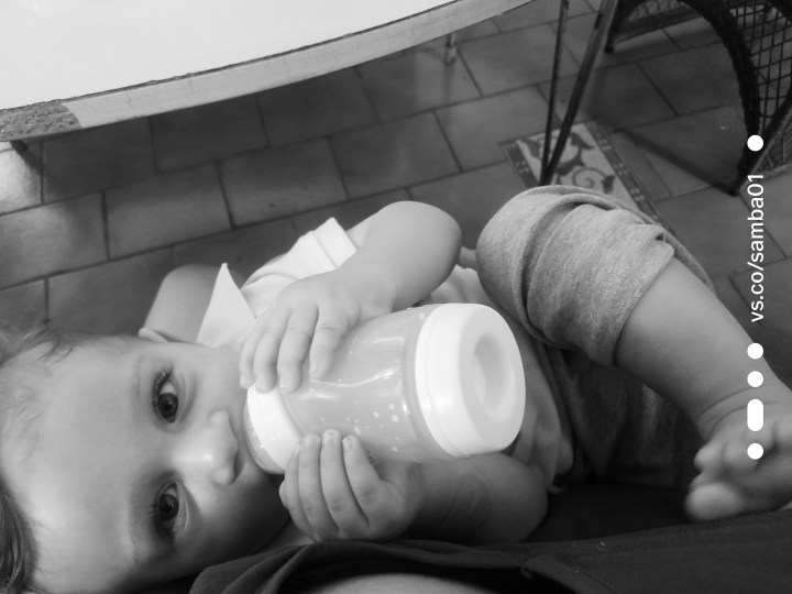 A black and white photograph of a baby drinking a bottle. 