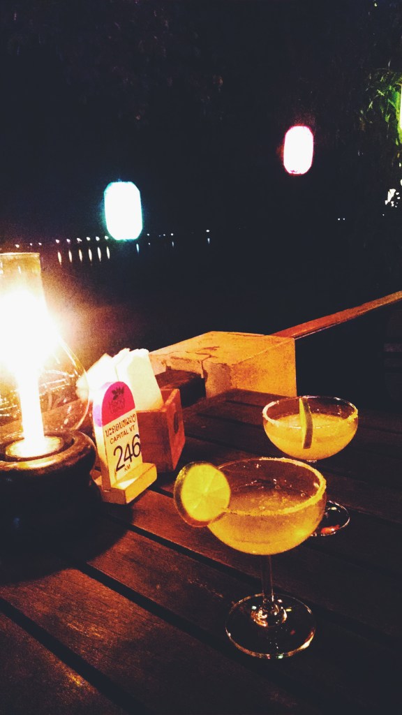Two margarita sit on a table illuminated by candles in the evening