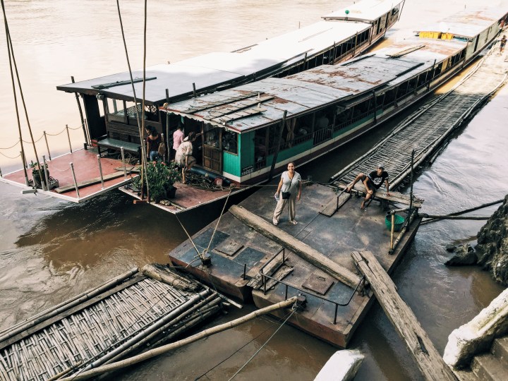 A woman stands on a dock in Laos looking up at the camera from far away