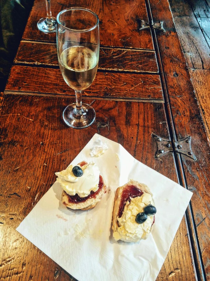 Two scones with jam, clotted cream, and topped with blueberries. A glass of champagne sits next to it. 