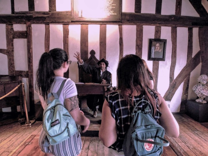 Two women with backpacks stand on line to meet the school master in Shakespeare's school house in Stratford Upon Avon