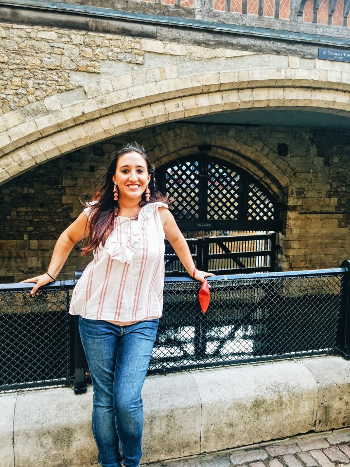 A woman in a white and pink striped shirt and jeans stands in front of Traitor's Gate at the Tower of London