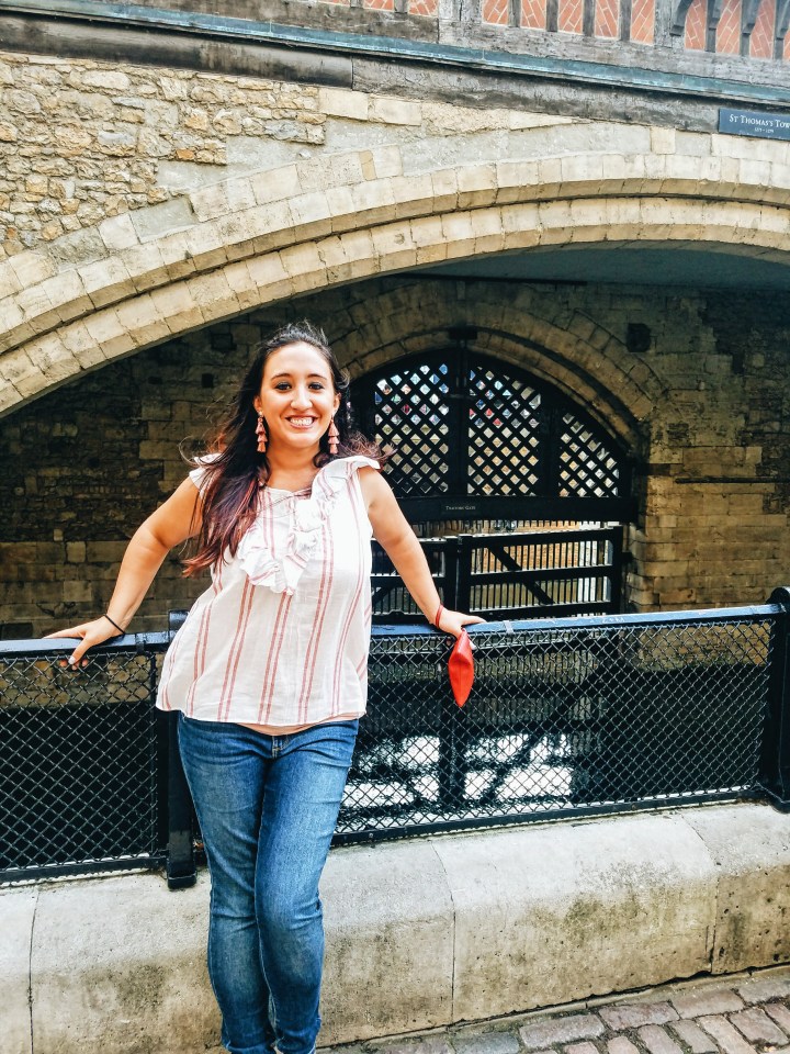 A woman in a white and pink striped shirt and jeans stands in front of Traitor's Gate at the Tower of London