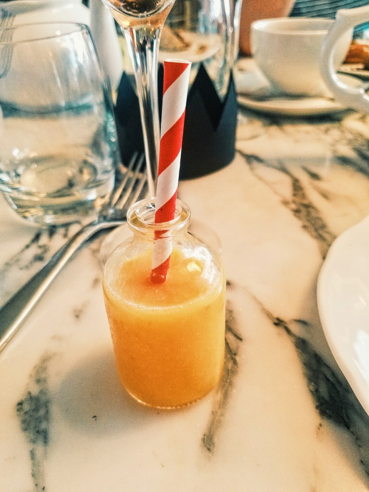 A small glass vile of Drink me, carrot meringue juice served at the Sanderson hotel's Mad Hatter Afternoon tea in London. It is orange, very small, and has a red and white straw