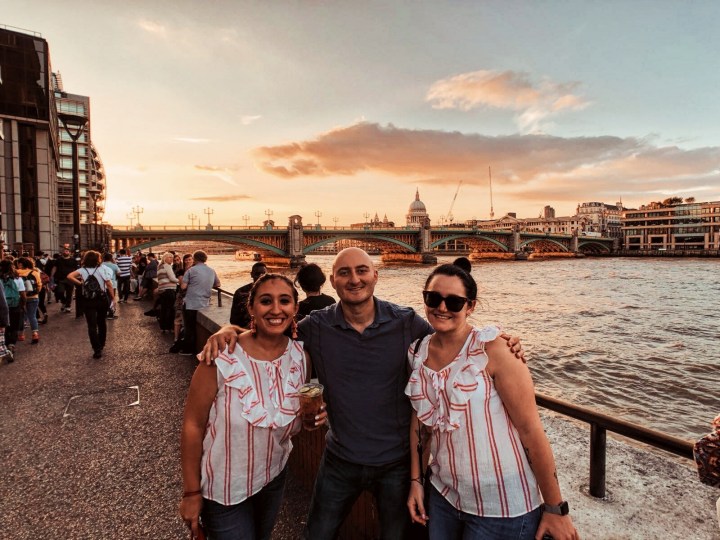 Photo of three people with the Thames and setting sun in the background. Definitely stroll along the Thames on your first visit to London.