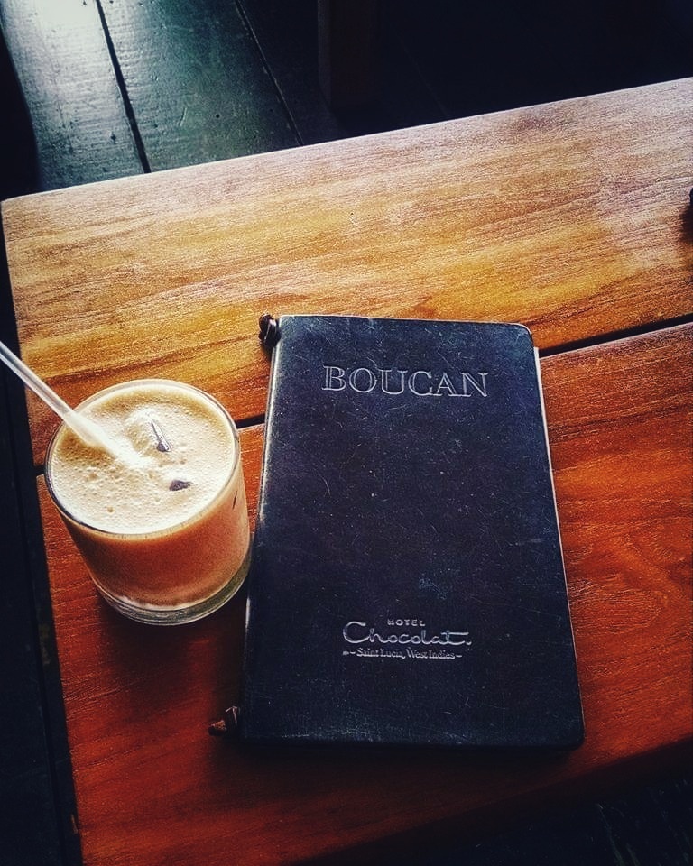Picture of black leather menu with words "Boucan" and "Hotel Chocolate" at bottom. Chocolate drink with straw in clear glass next to it. The best place to eat if you have limited time, like one day in Soufriere. 