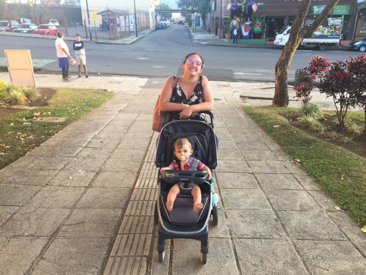 A mother in sunglasses wheels her baby around in a stroller through the streets of San Jose, Costa Rica.