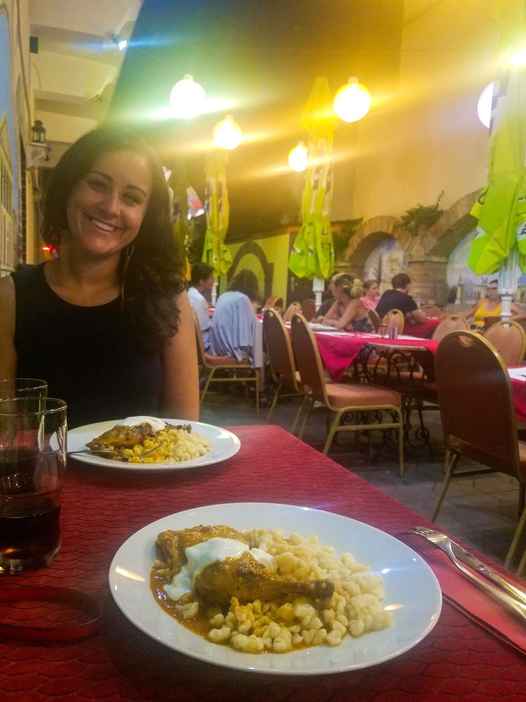 Two plates of chicken paprikash in Budapest, Hungary. A woman with a black sleeveless top and brown hair smiles at the camera. 