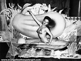 A burlesque performer, Kitty West AKA Evangeline the Oyste Queen is picture in a giant oyster shell while wearing a bikini.