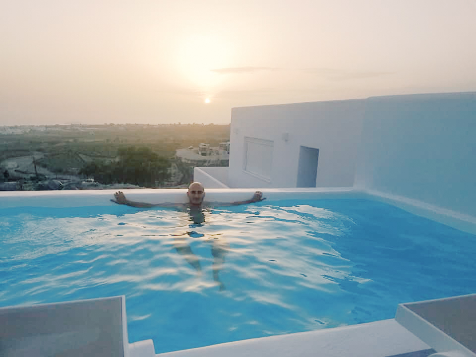 A man in a pool in Santorini at sunset