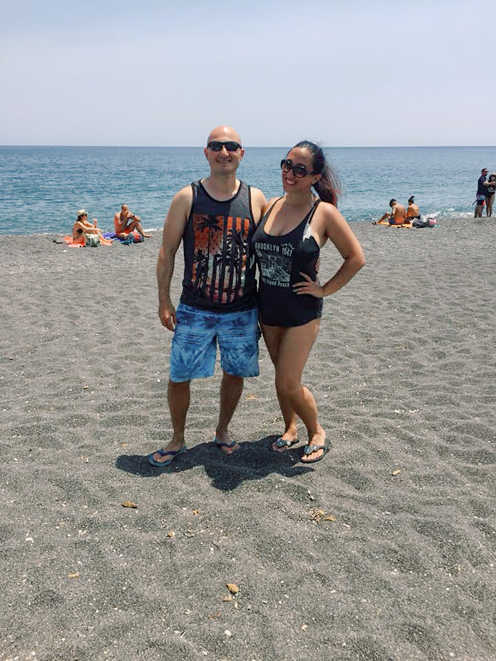 A couple poses on a beach in Santorini