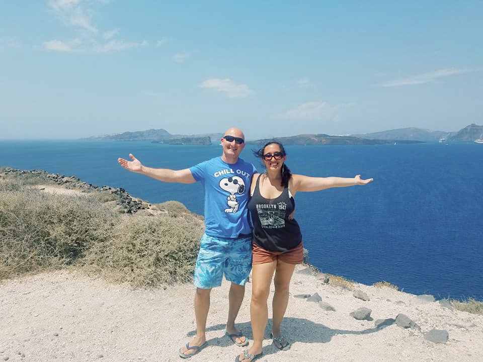 A couple poses on a cliff overlooking the ocean in Santorini