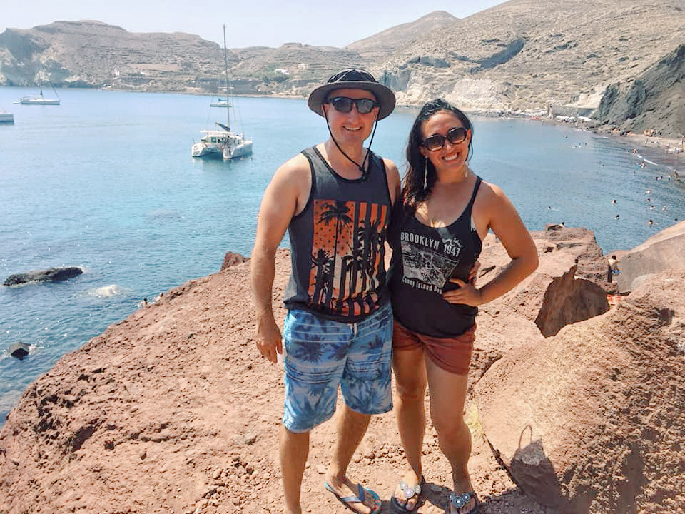 Couple poses standing on the cliffs overlooking the ocean in Santorini