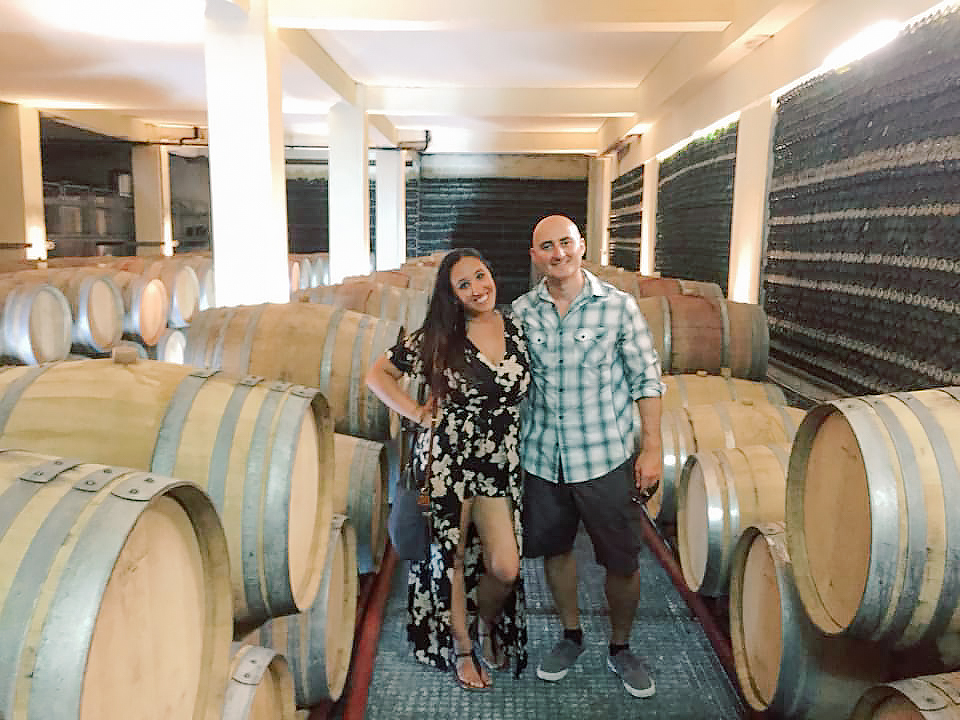 A couple poses next to barrels of wine in Santorini