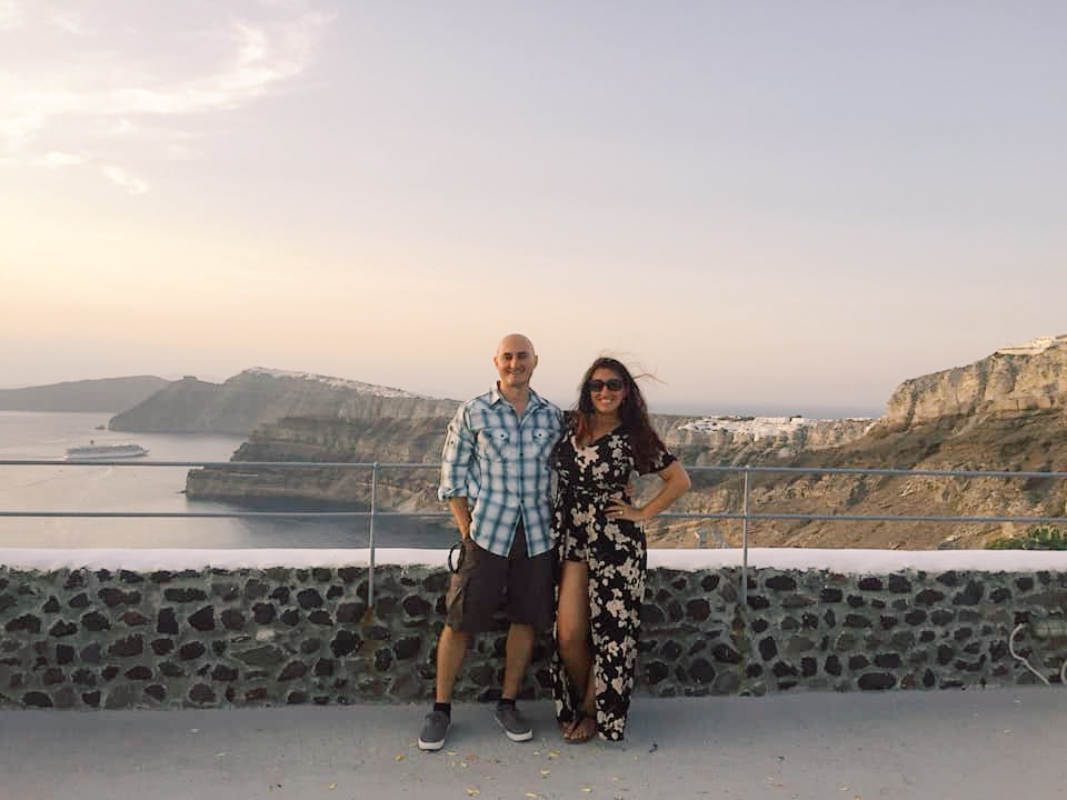 A couple posing in front of a backdrop of Santorini and the cliffs along the shore