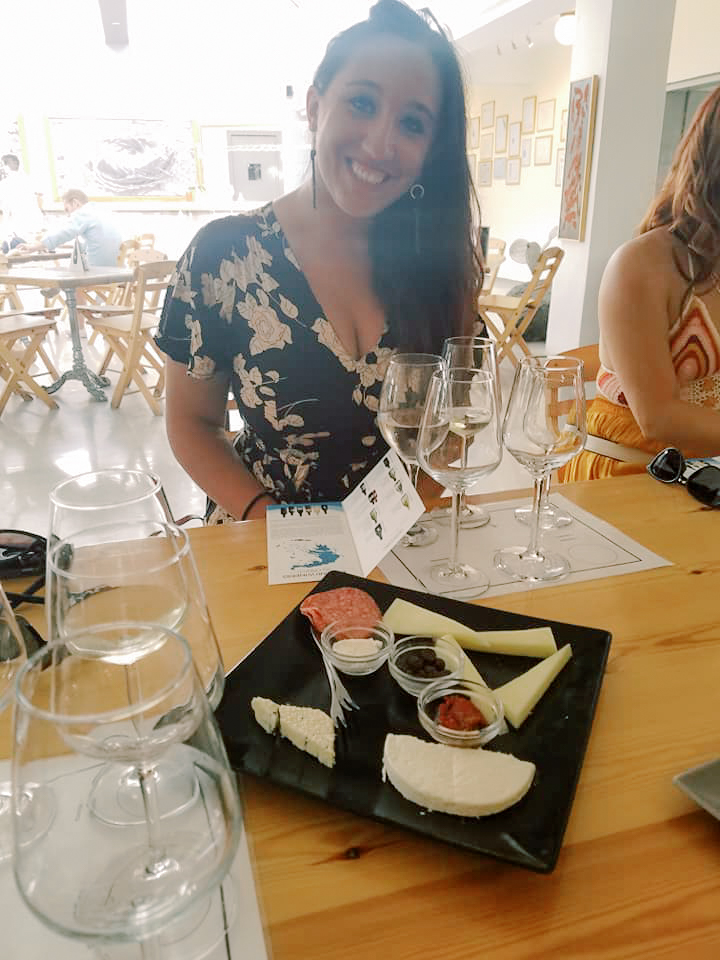 A woman sits at a table filled with snacks at a wine tasting 