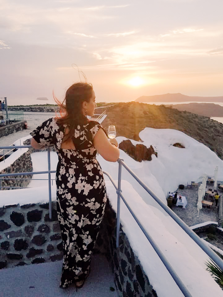 A woman looks out over a sunset at a winery in Santorini