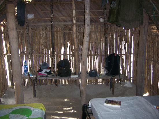 The interior of a hut, the floor is sand and the hut is held up by wooden poles