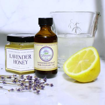 A jar of lavender honey and lavender extract next to a glass of water and a lemon