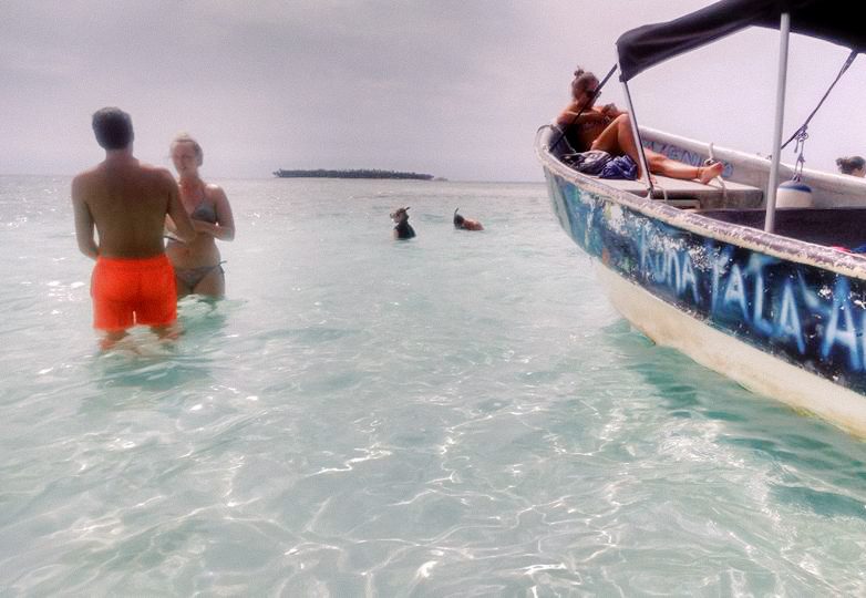 People standing and swimming in the water beside a tourist boat