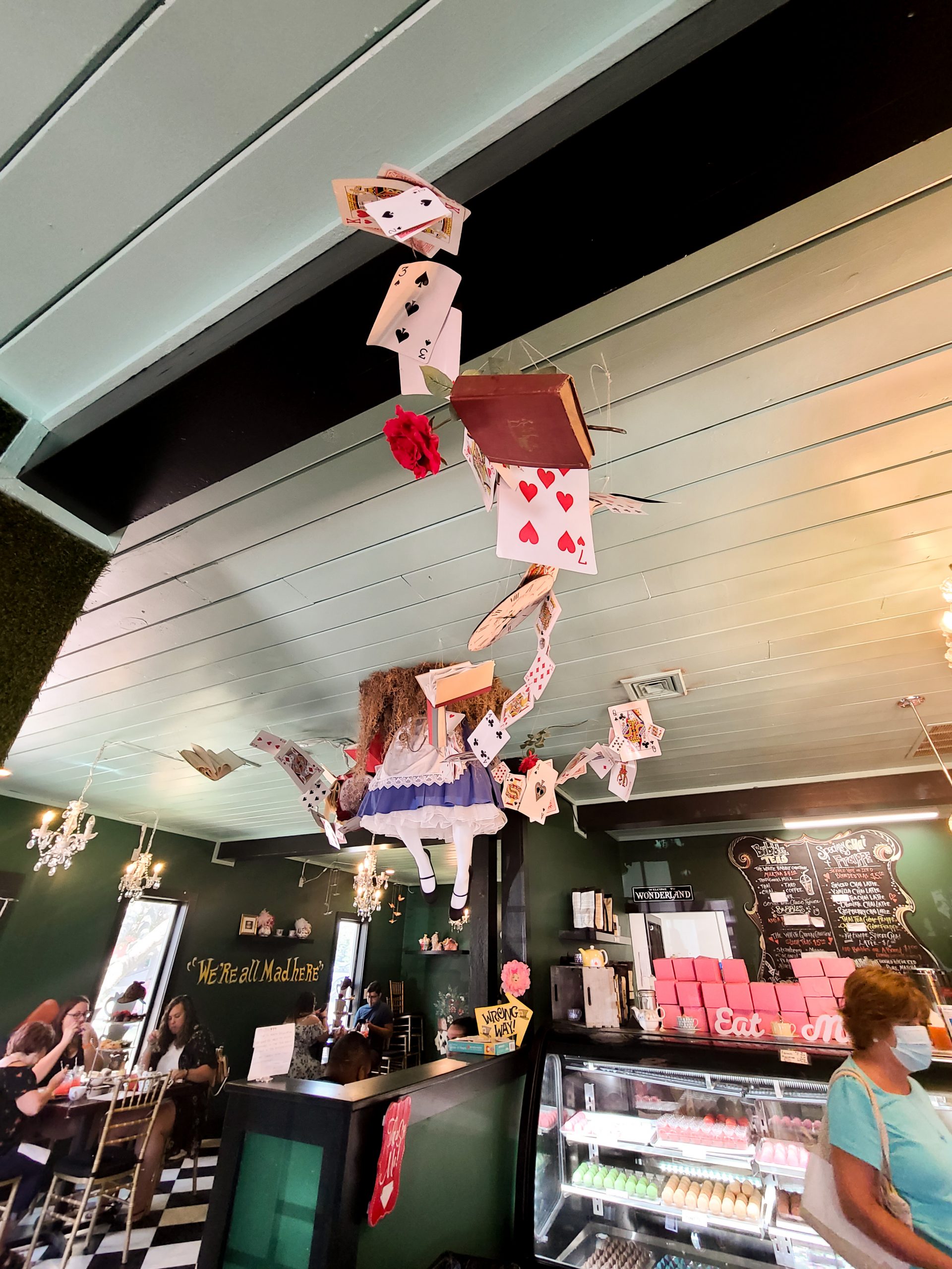 A photo of a decoration inside an Alice in Wonderland themed shop that is made to look as though Alice is falling through the shop's ceiling