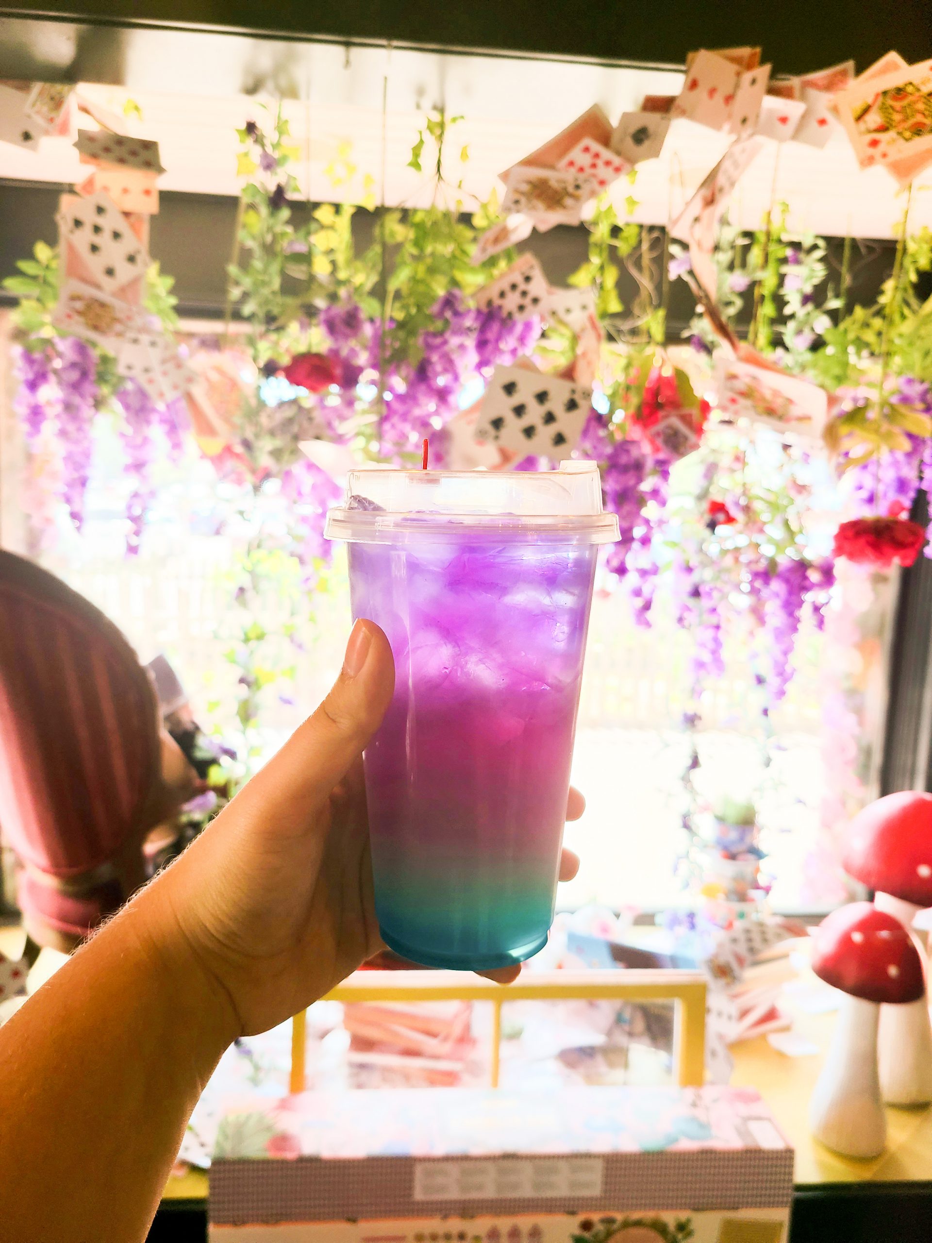 A colorful beverage held up against the backdrop of the Alice in Wonderland shop
