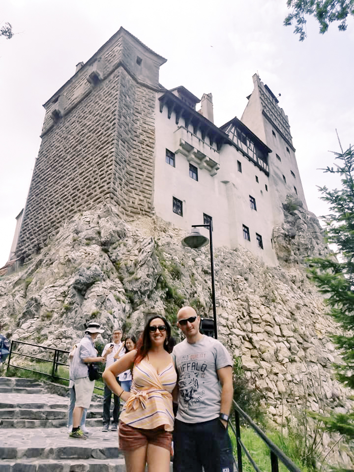 A man and a woman pose in front of Bran castle in Romania