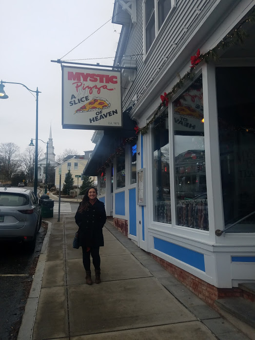 A woman stands underneath the sign for Mystic Pizza in Mystic, Connecticut
