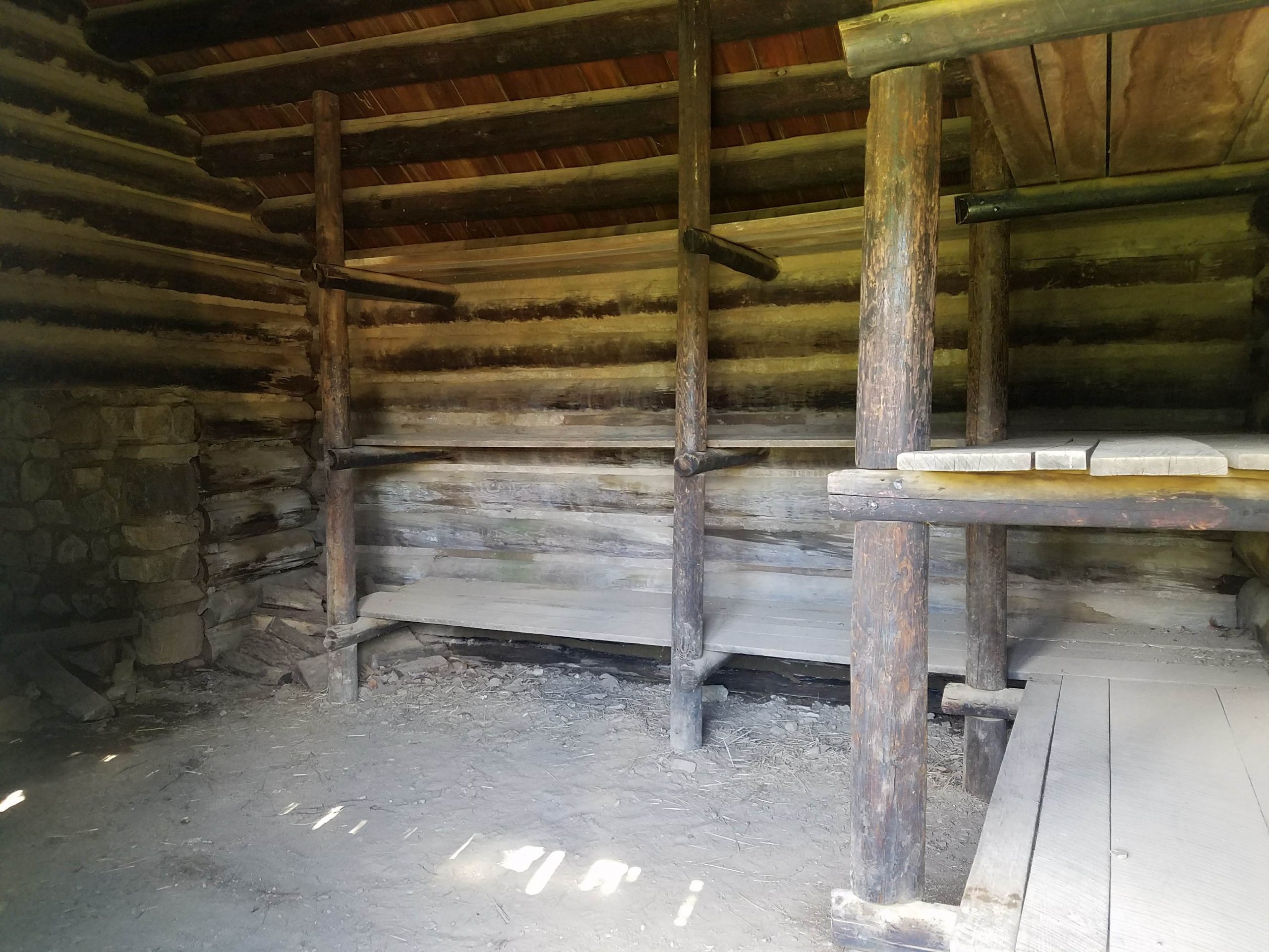 A photo of the wooden plank beds and dirt floor inside of the wooden cabins