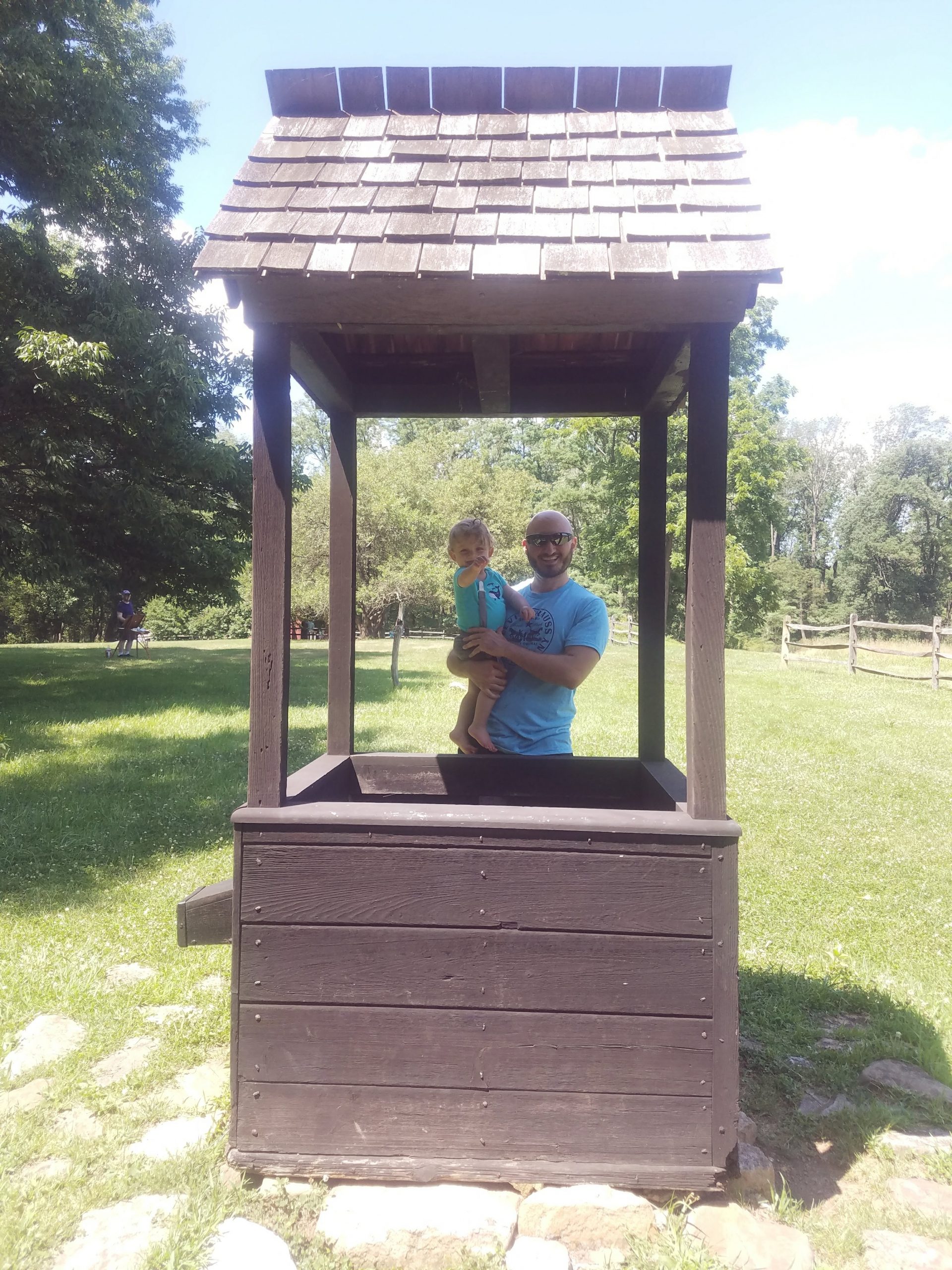 A man and child stand beside a wooden well 