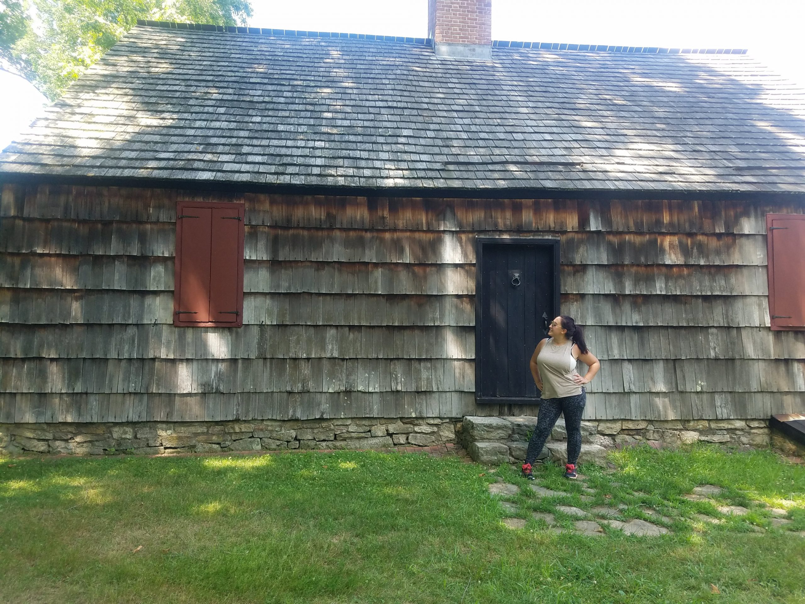 A woman stands outside of a wooden cabin in Jockey Hollow Park