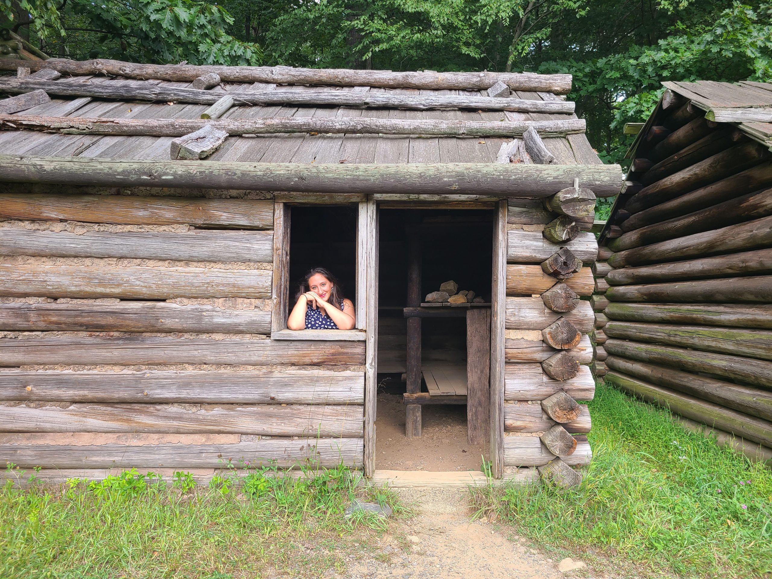 A woman looks out the window of a wooden cabin