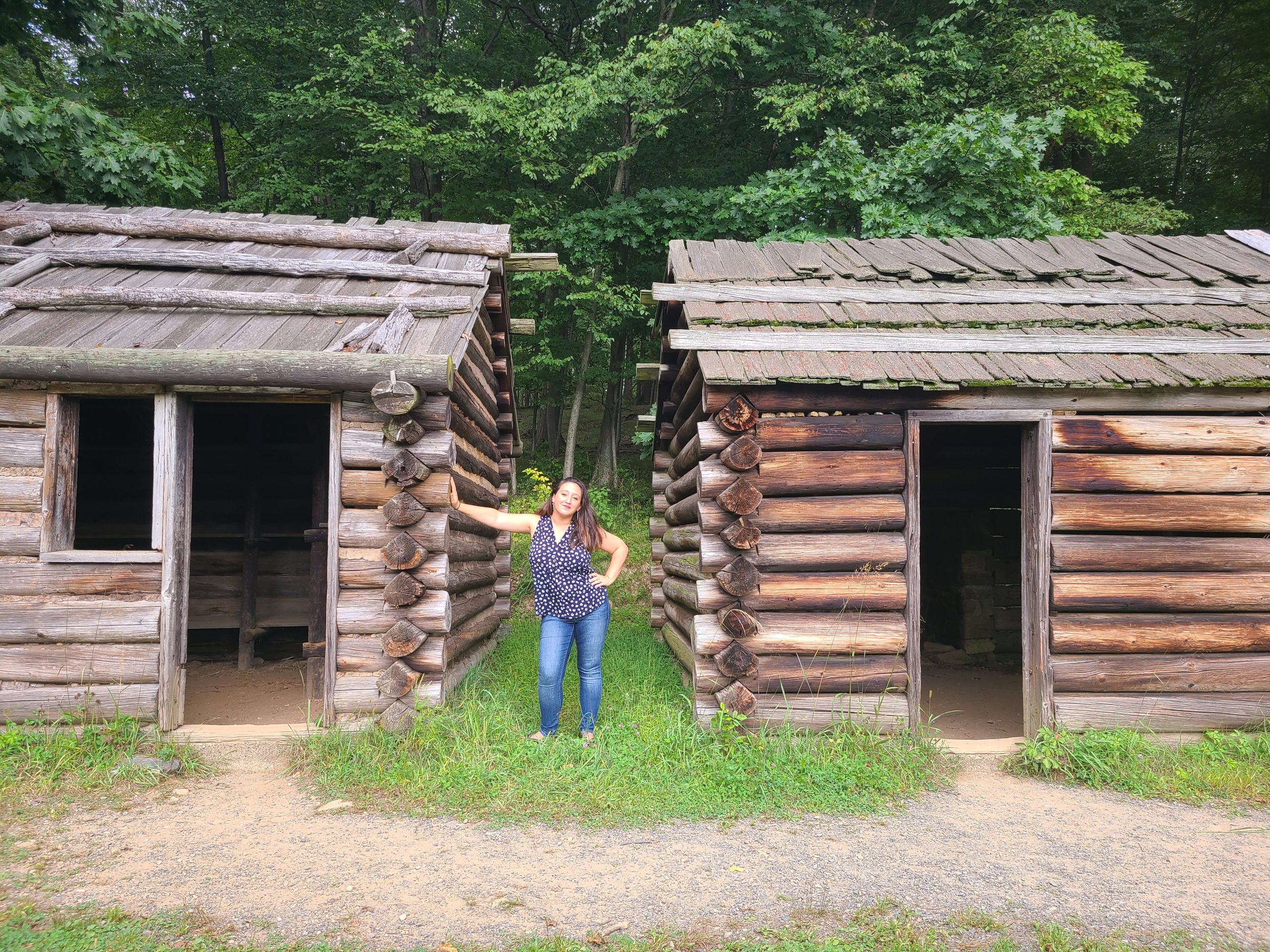 A woman poses inbetween two cabins in Jockey Hollow Park