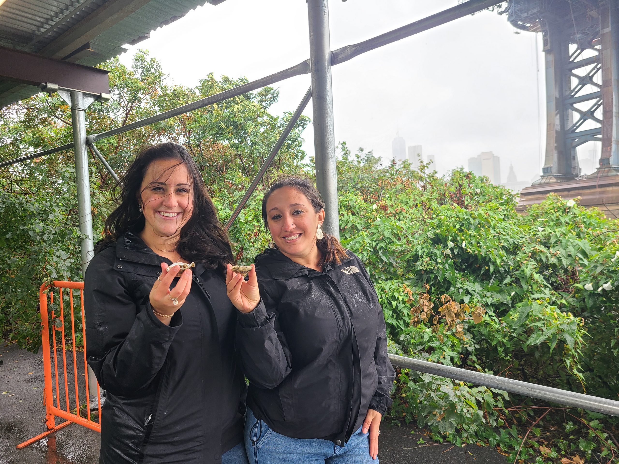 Two women pose while holding up oysters