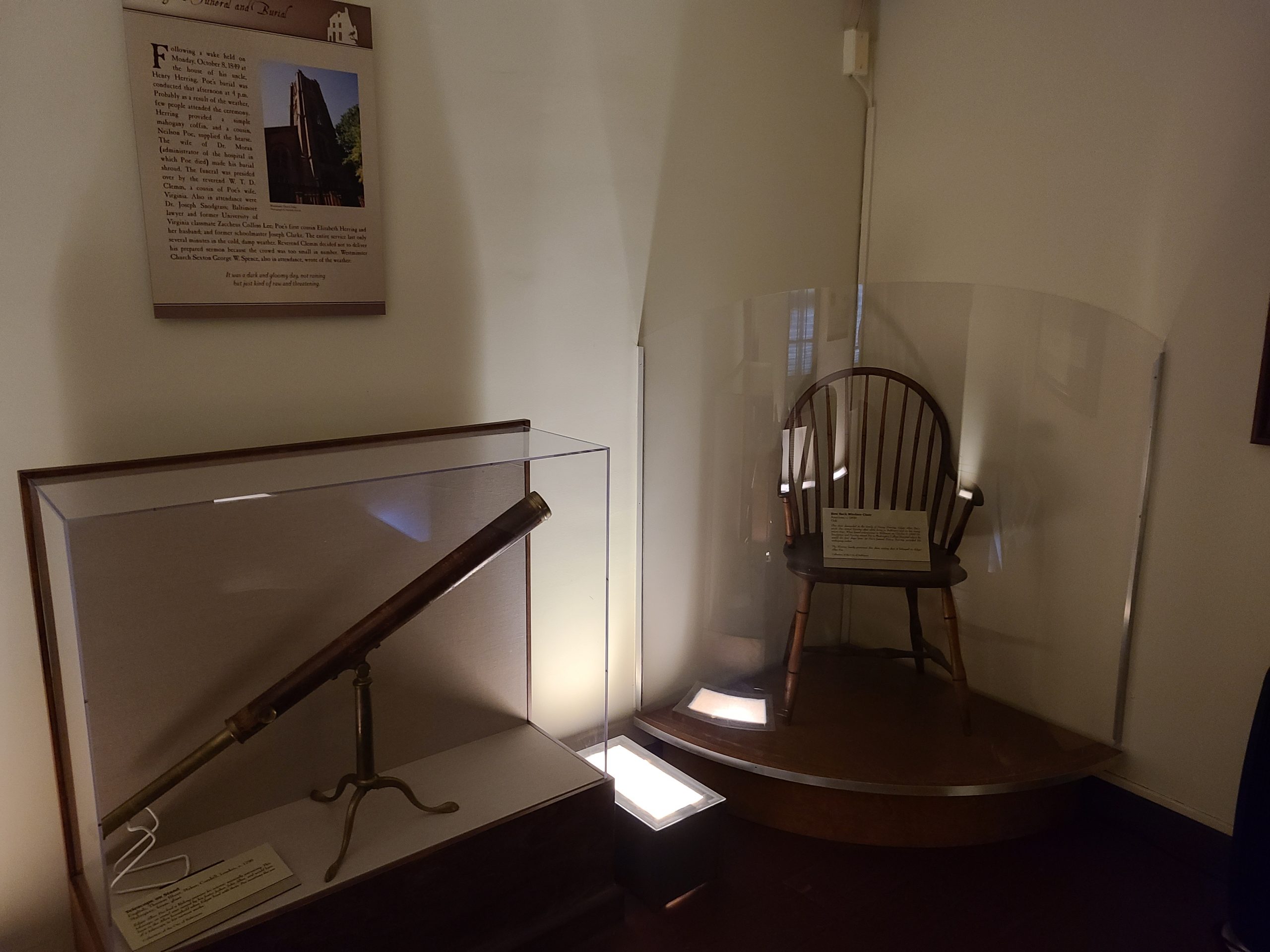 A rocking chair and telescope protected in glass cases in the Edgar Allan Poe museum