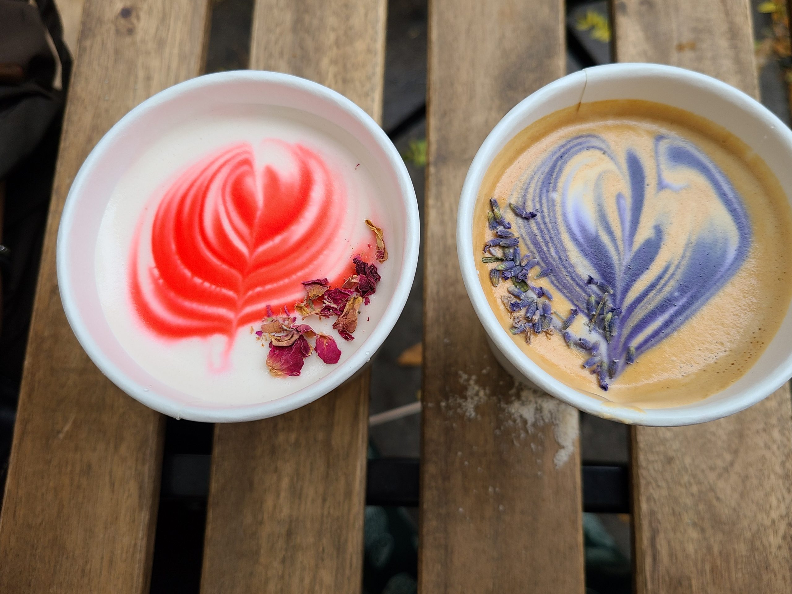 Two cups of coffee with colorful latte art and floral petals.