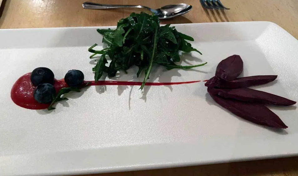 An appetizer plate of wtih four slices of smoked puffin and some greens